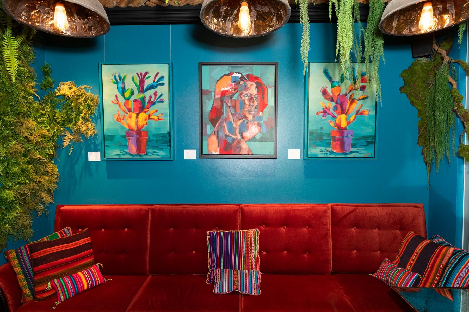 Colourful paintings by Brad Kenny hung on a teal wall above a red sofa at COYA City