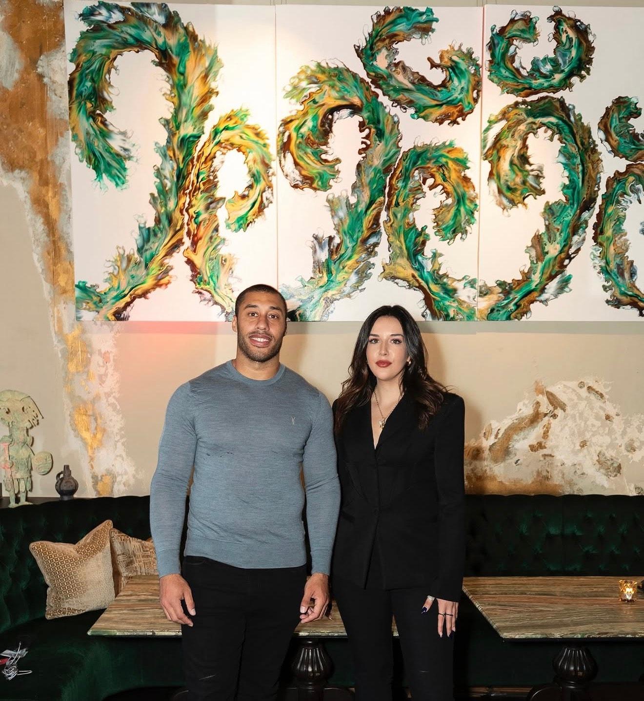 Two guests posing in front of a green sculptural wall installation, part of The COYA Art Programme