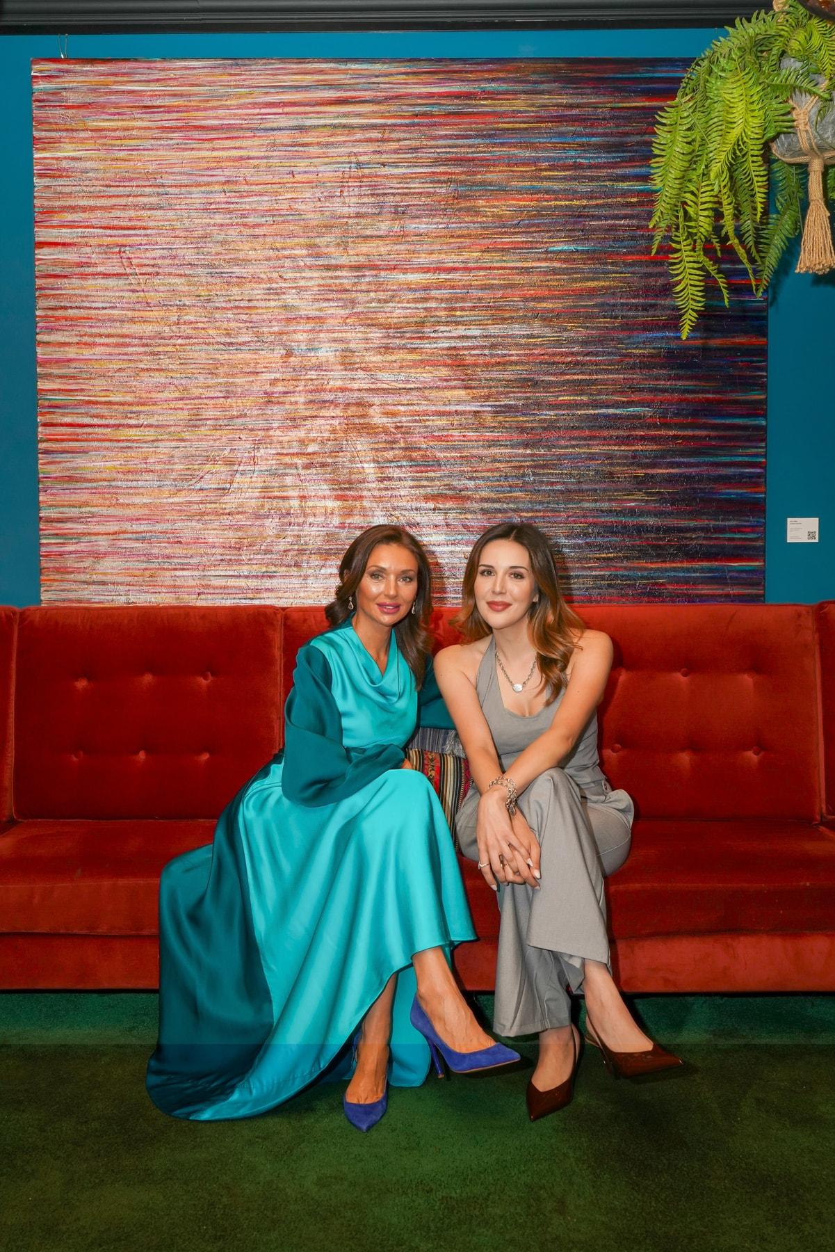 Two women seated on a red sofa in front of a large striped abstract painting by Lara Julian at COYA City